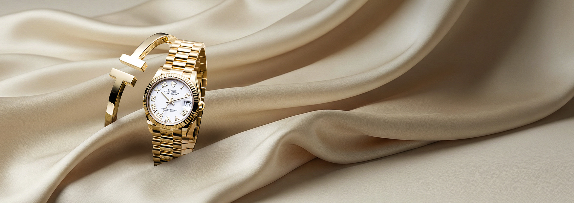 Goldenes Armband und goldene Luxusuhr auf glänzendem Stoff